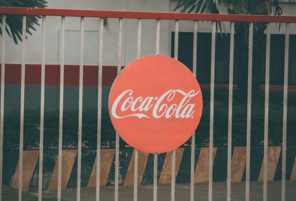 Coca-Cola logo prominently displayed on outdoor fence, urban setting.